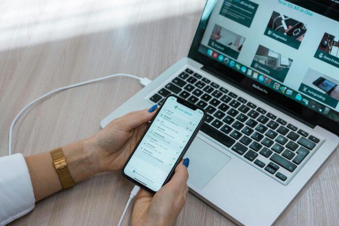seseorang menggunakan ponsel sambil duduk di depan laptop