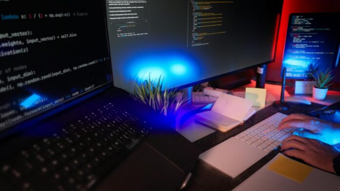 Pengkodean programmer di meja dengan beberapa monitor.