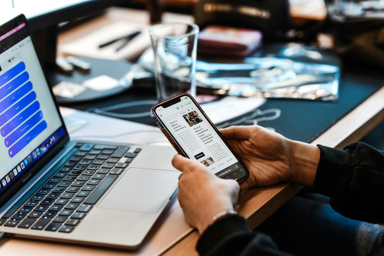 seseorang yang duduk di meja dengan laptop dan ponsel